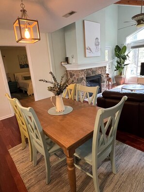 A dining area with a wooden table, four chairs, a vase with plants, and a hanging light fixture. - Tranquil Waters, OceanPines, 3 br, Dog Friendly (Ocean Pines)