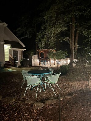 An outdoor patio with a table and chairs, a wooden pergola, and a white picket fence.