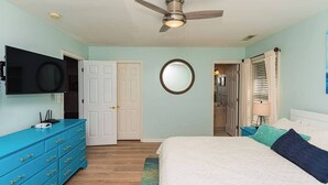 Un dormitorio con cama, ventilador de techo, televisor, cómoda y una puerta.