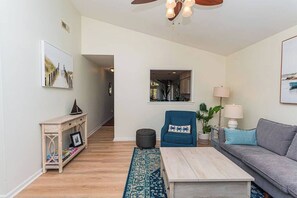 A living room with a sofa, a coffee table, a blue armchair, a lamp, and a console table with a picture frame. - Tranquil Waters, OceanPines, 3 br, Dog Friendly (Ocean Pines)