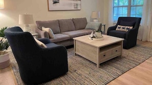 En stue med sofa, to lænestole, sofabord og et billede på væggen.