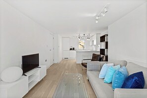 Una sala de estar moderna con un televisor de pantalla plana, un sofá con cojines estampados y una mesa de centro de vidrio.