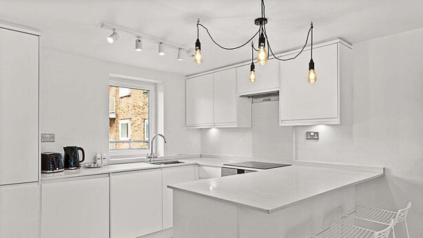 Una cocina moderna con armarios blancos, una isla central e iluminación colgante.