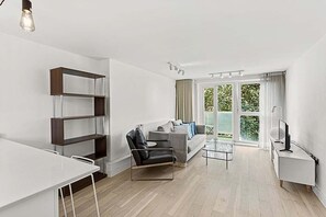 A modern living room with a sofa, a coffee table, a bookshelf, and a TV stand. - Belgravia Living – 2-Bed, 2-Bath Fourth Floor Apartment (London)