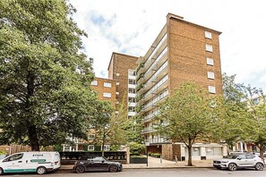 Un edificio residencial de varios pisos con fachada de ladrillo, balcones y un estacionamiento con automóviles.