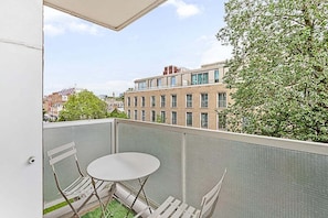 Un balcon avec une table et des chaises, une vue sur des immeubles et un arbre.