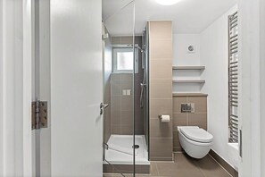Un baño moderno con ducha de mampara de vidrio, inodoro y toallero.