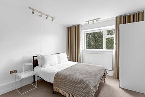 Un dormitorio con cama, mesita de noche, ventana con cortinas y armario.