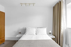 Une chambre d’hôtel avec un lit, des tables de chevet blanches, une armoire en bois et une fenêtre avec des rideaux.