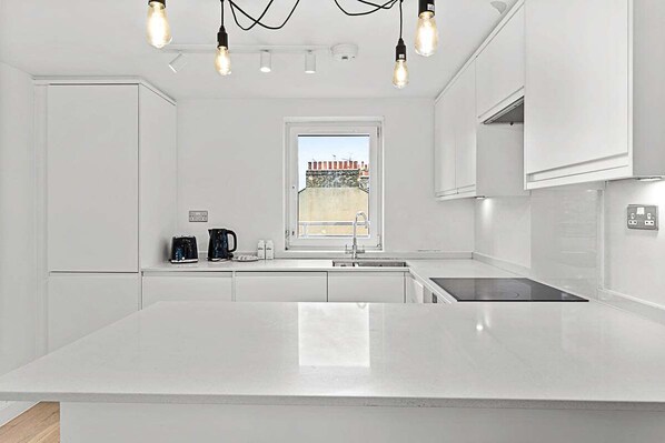 Una cocina moderna con armarios blancos, una isla central, una estufa integrada y un ventanal con vistas a edificios.