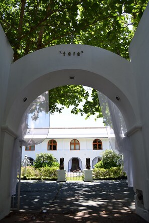 An arched entrance with a white wall, a building with arched windows, and greenery in the background. - Junior Suite con Terraza (Cozumel)