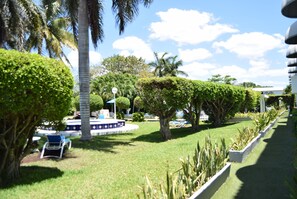A well-maintained garden with neatly trimmed hedges, palm trees, and a circular seating area with a fountain. - Junior Suite con Terraza (Cozumel)