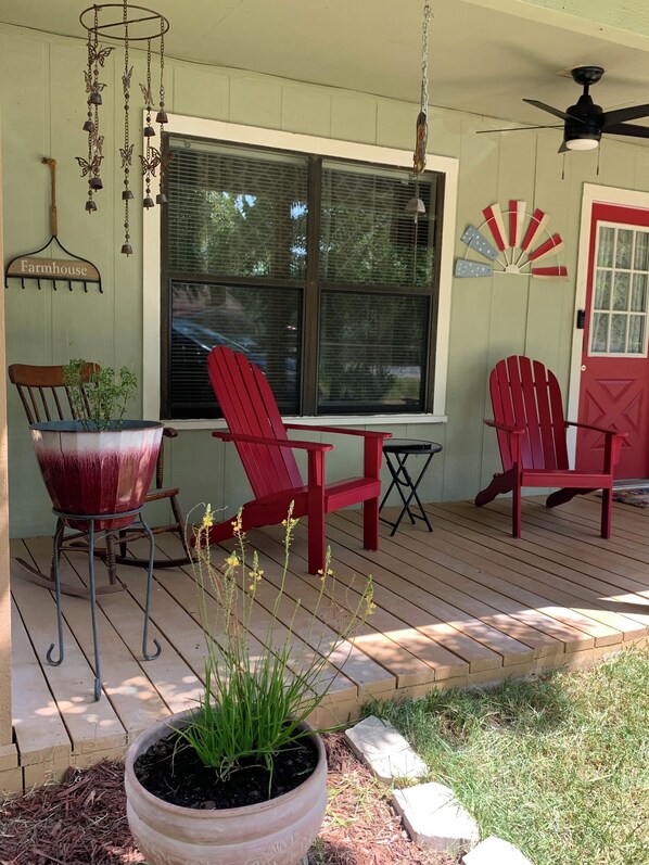 A porch with red Adirondack chairs, a rocking chair, and a potted plant.