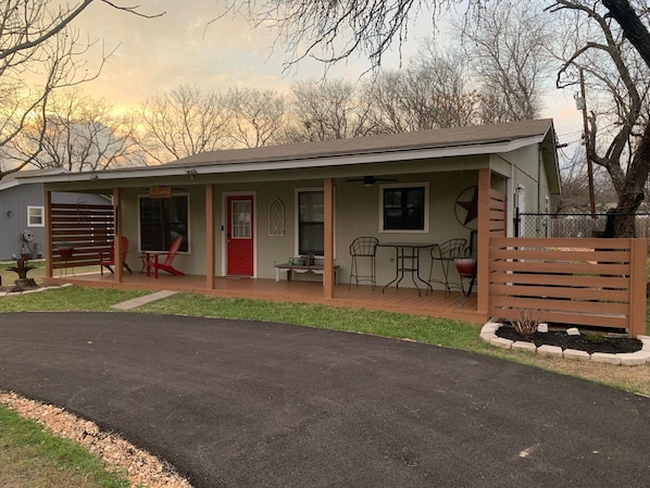 A single-story building with a covered porch, a red door, and a small patio area with outdoor furniture.