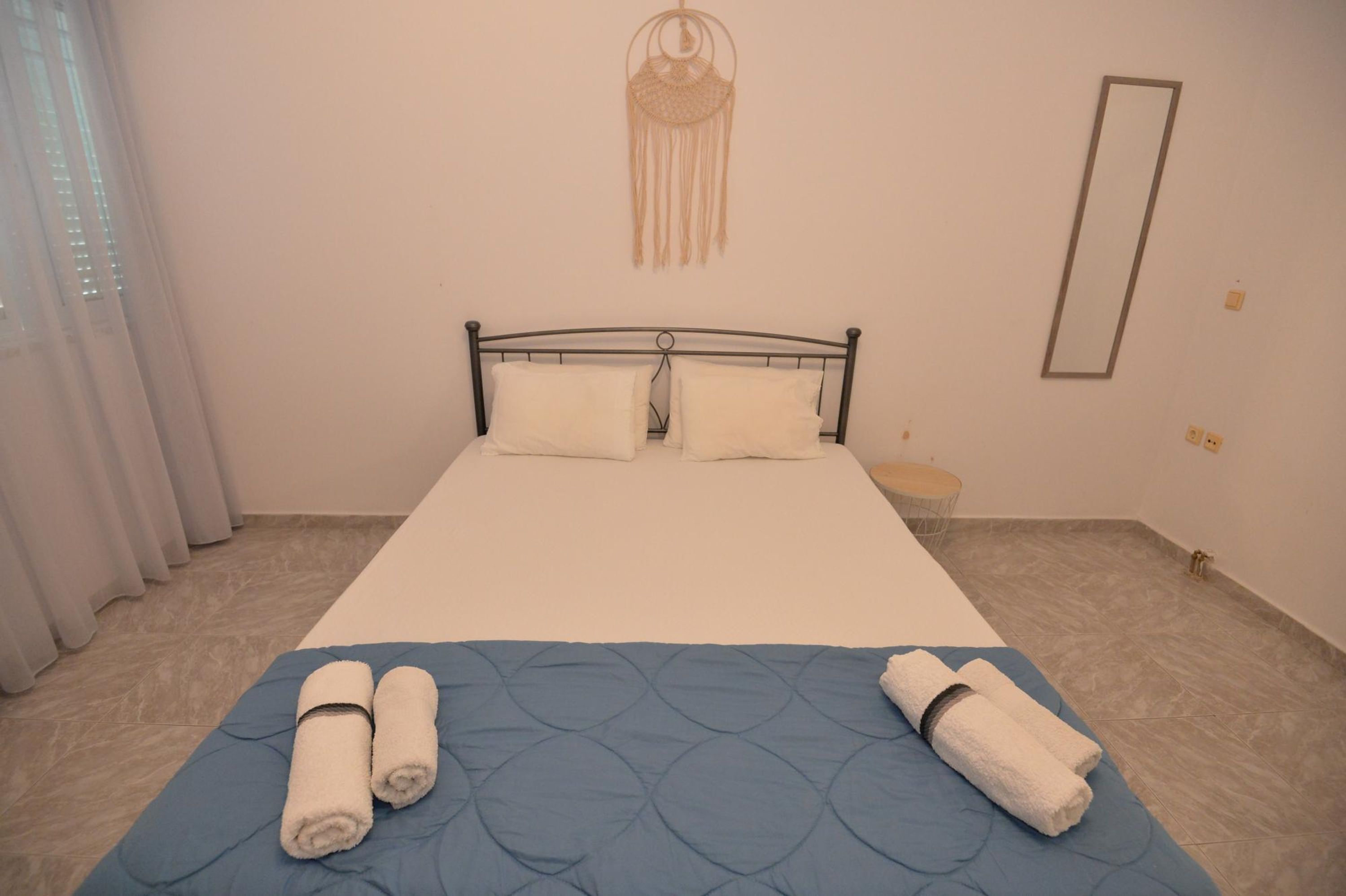 Un letto rifatto con una coperta blu, due asciugamani arrotolati, un'acchiappasogni appeso al muro e uno specchio.