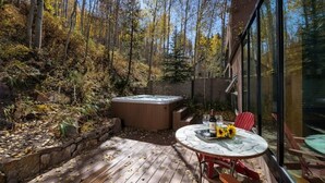 A wooden deck with a hot tub, a table with chairs, and a glass-enclosed patio. - Vail Ski Home next to National Forest (Vail)