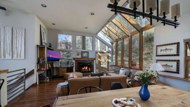 A spacious living room with a fireplace, a dining area with a wooden table, and large windows offering a view of the outdoors. - Vail Ski Home next to National Forest (Vail)