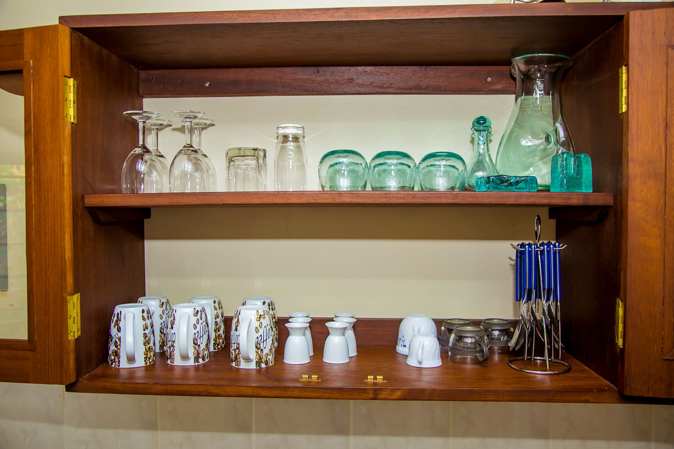 A wooden shelf with various glassware and ceramic mugs.