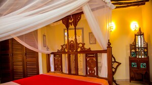 Una cama con colcha roja y dosel, muebles de madera y una lámpara fijada a la pared.