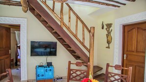 Un comedor con escalera de madera, televisor montado en la pared y una mesa con mantel estampado en azul.