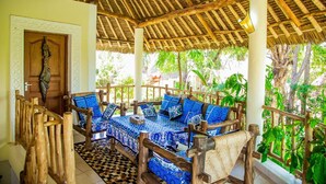 Un espacio de estar al aire libre cubierto, con mobiliario de madera y cojines estampados, rodeado de exuberante vegetación.