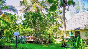 Un jardín exuberante con palmeras, una estructura de techo de paja y un césped bien cuidado.