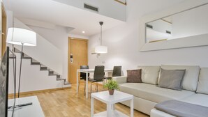 A modern living room with a sofa, a coffee table with a plant, a dining table with chairs, and a staircase. - Inside Barcelona Apartments Princep (Barcelona)