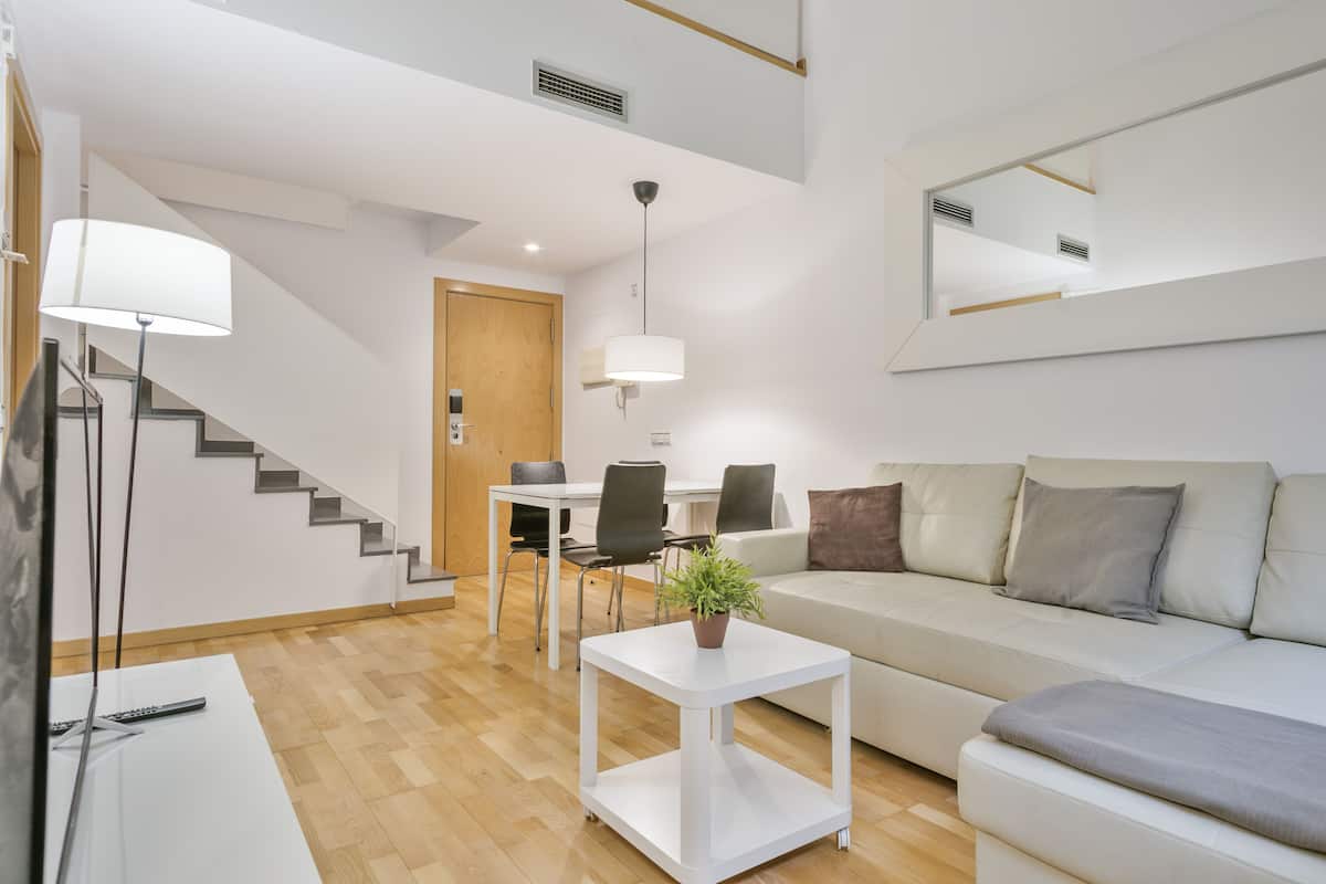 A modern living room with a sofa, a coffee table with a plant, a dining table with chairs, and a staircase.