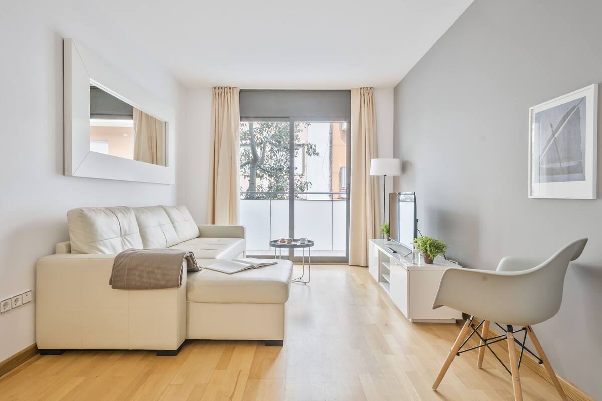 A modern living room with a sofa, a dining area with a chair, a small table, and a view of the outside.