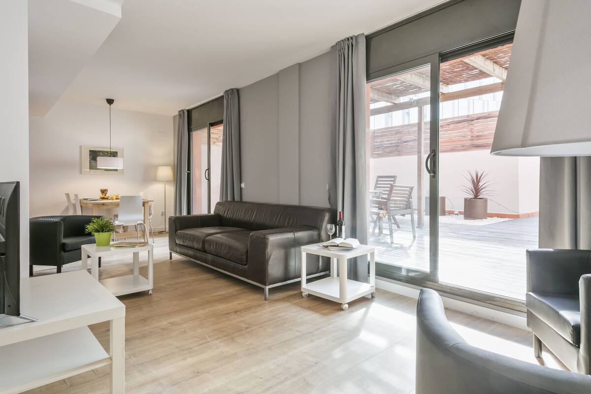 A modern living room with a leather sofa, a white coffee table, and a glass door leading to an outdoor patio.
