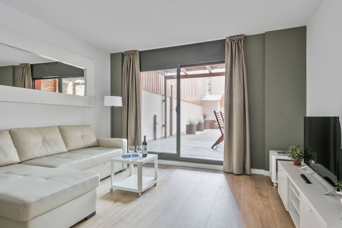 A modern living room with a sofa, a coffee table, a TV, and a sliding glass door leading to an outdoor area.