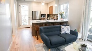 A modern kitchen with a central island, a dark sofa with a patterned pillow, and a dining area with chairs. - NEW Hip & Stylish House 30 steps from South Congress
 (Austin)