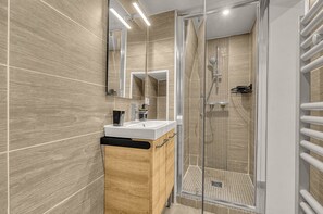 A modern bathroom with a glass-enclosed shower, a wooden vanity, and a large mirror.