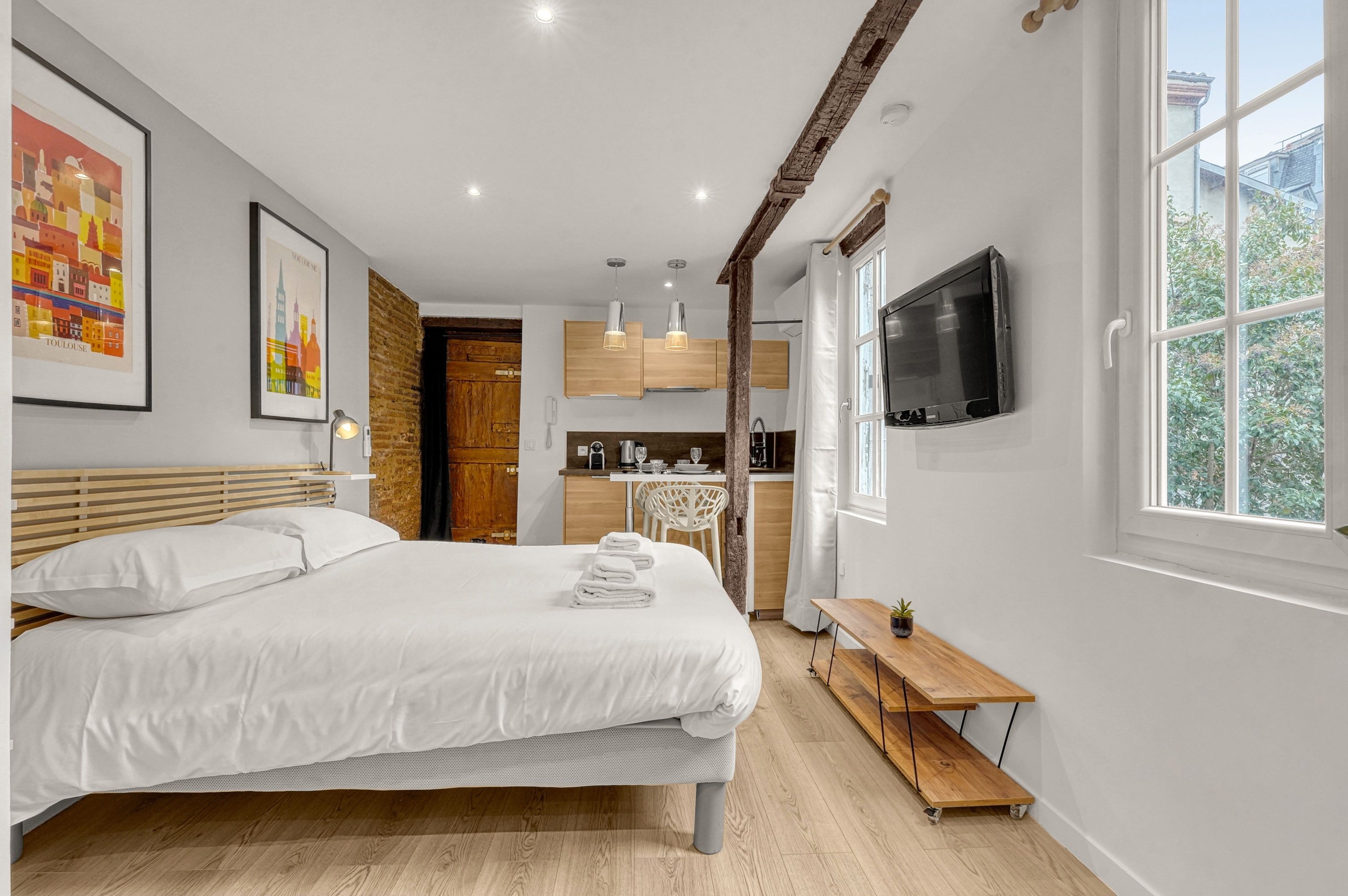 Une chambre moderne avec un grand lit, une tête de lit en bois, une table de chevet agrémentée d’une plante et un téléviseur fixé au mur.