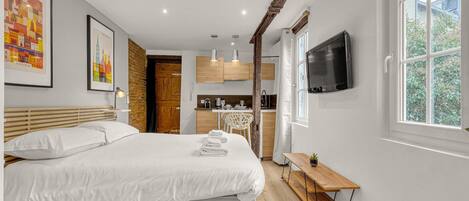 Un dormitorio moderno con una cama grande, un cabecero de madera, una mesita de noche con una planta y un televisor montado en la pared.