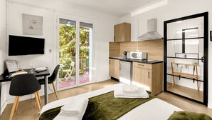 Ein modernes Hotelzimmer mit Bett, Schreibtisch mit Stuhl, einer Küchenzeile und einer Glastür, die auf einen Balkon führt.