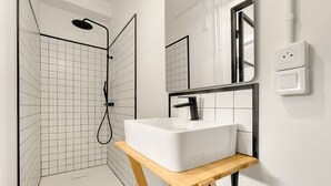 Ein modernes Badezimmer mit Dusche, einem weißen Waschbecken auf einem Holzschemel und einem Spiegel darüber.