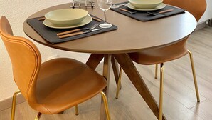 A dining area with a round table, two chairs, and a window in the background.
