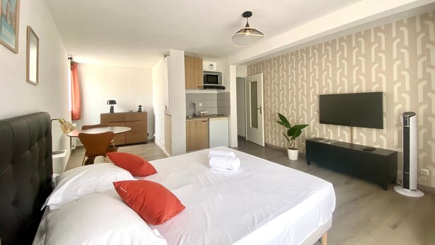 A hotel room with a bed, a desk, a microwave, a TV, and a plant.