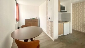 A compact kitchen with a microwave, a refrigerator, and a small countertop. There is a wooden dining table with chairs.