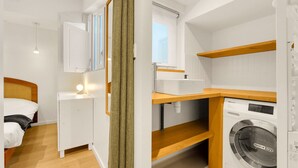 Ein kompakter, moderner Raum mit Bett, Nachttisch und Waschmaschine.