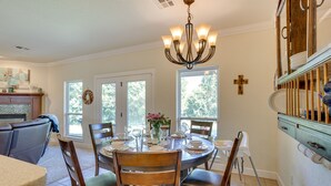 A dining area with a chandelier, wooden chairs, a round table, and a view of the outdoors through large windows. - Quaint Noble Home: 6 Mi to University of Oklahoma! (Noble)