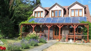 A house with solar panels, a covered porch, and a garden with flowers and shrubs. - Sunnyside Cottage - Rural 2-bedroom apartment (Bristol)