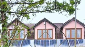 A house with a pink facade, a covered porch with solar panels, and a gated entrance. - Sunnyside Cottage - Rural 2-bedroom apartment (Bristol)