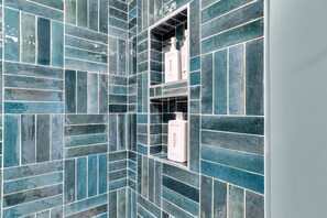 Une salle de bain avec des murs recouverts de carreaux bleus et une étagère sur laquelle se trouvent deux bouteilles étiquetées « Native ».