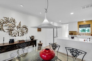 Une cuisine moderne avec des meubles blancs, une table à manger en verre et un vase rouge.