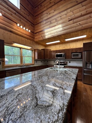 Une cuisine moderne avec des murs en bois, un grand îlot en granit, des appareils électroménagers en acier inoxydable et une fenêtre offrant une vue sur l’extérieur.