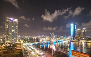 A nighttime cityscape with illuminated buildings, a bridge, and a river reflecting the lights. - Capital O 1200 Salem Riverside Hotel (Da Nang)