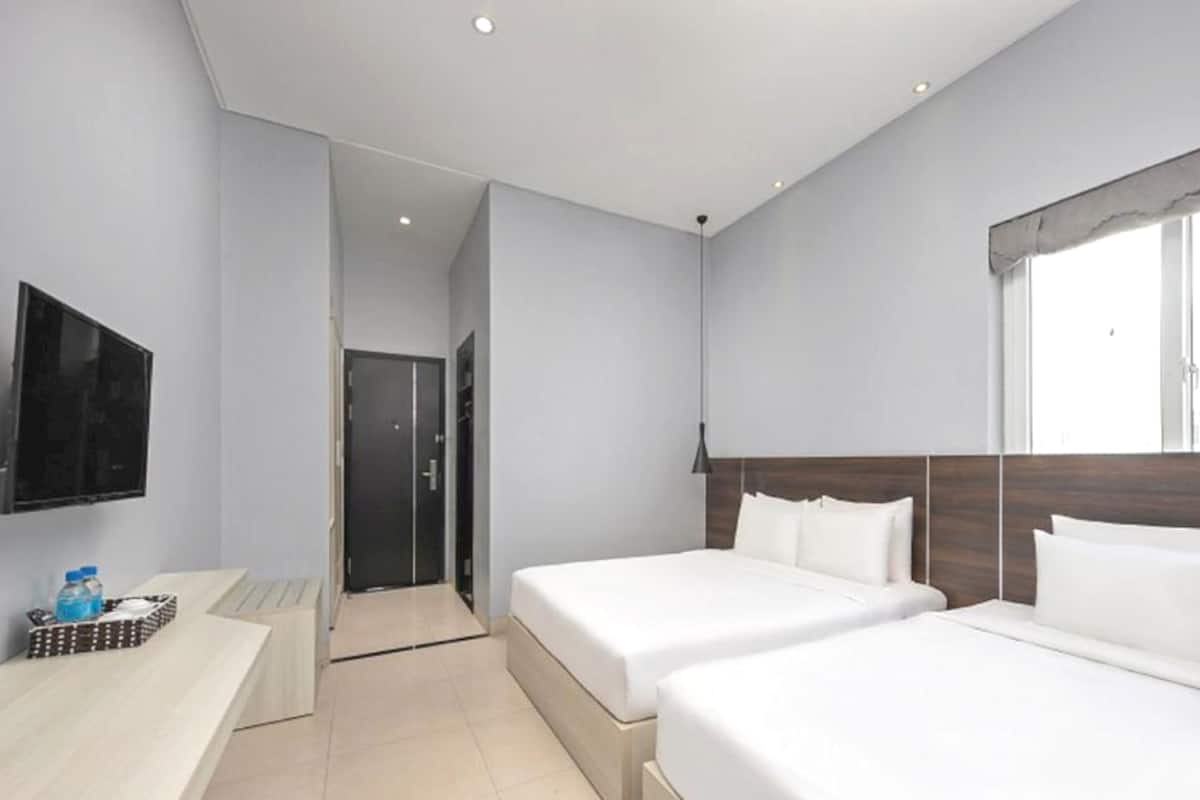 A hotel room with two beds, a TV, a desk, and a window.