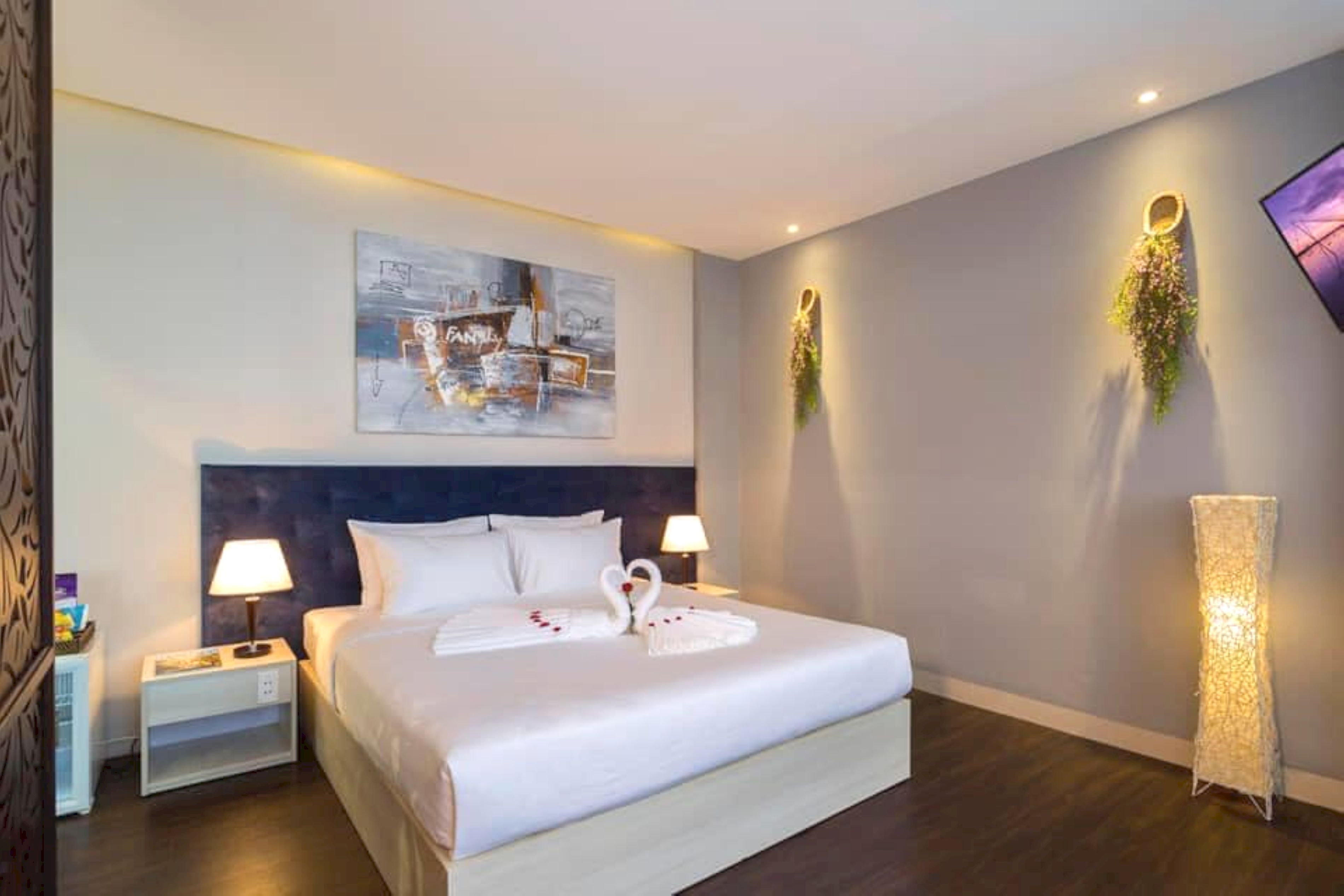 A hotel room with a large bed, two bedside tables with lamps, a wall-mounted artwork, and a floor lamp.